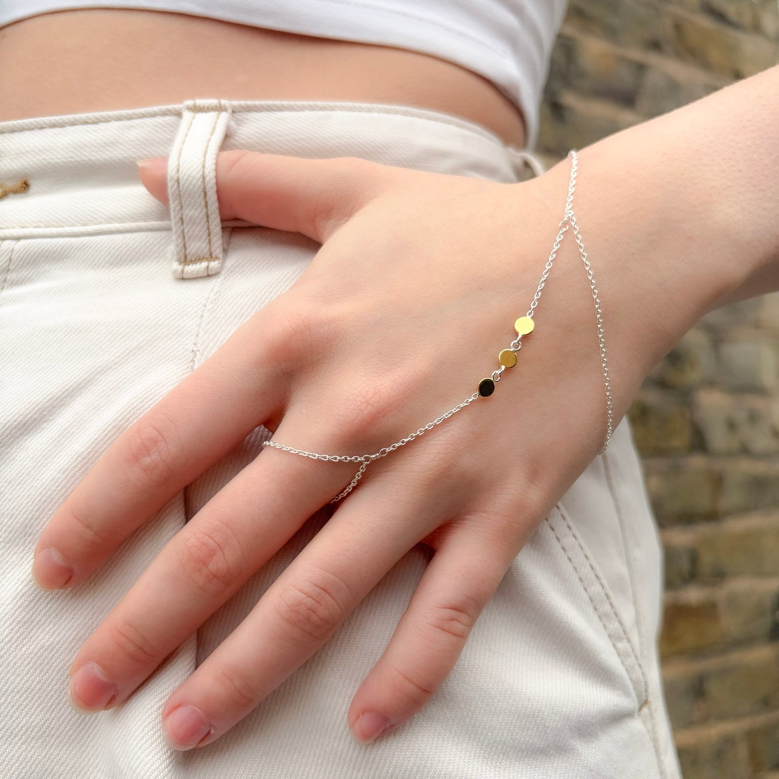 Hand wearing a delicate silver bracelet with small beads against a neutral background