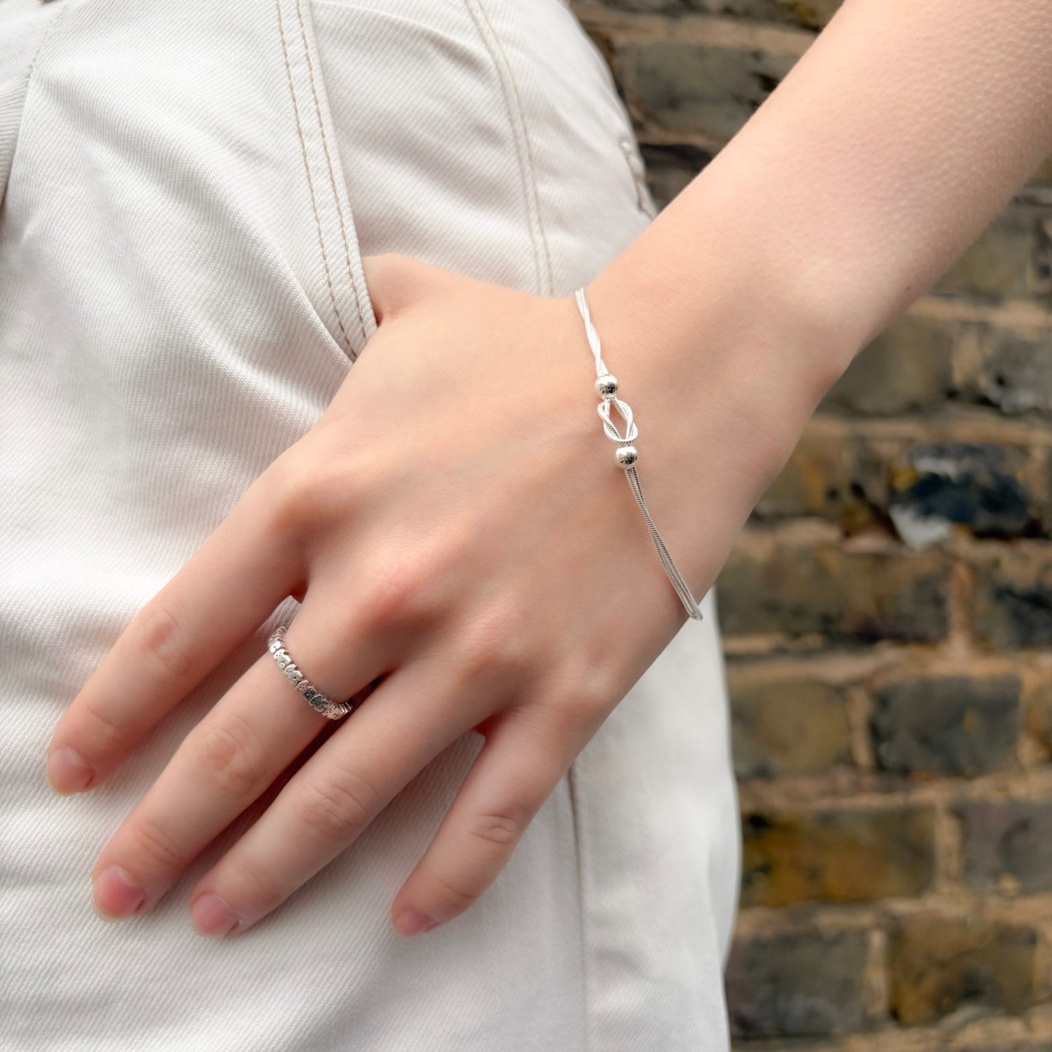 Hand wearing a silver bracelet with a brick wall background