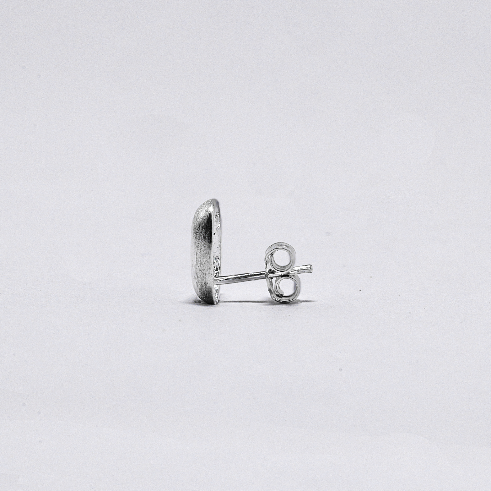 Silver earring side view on a light grey background