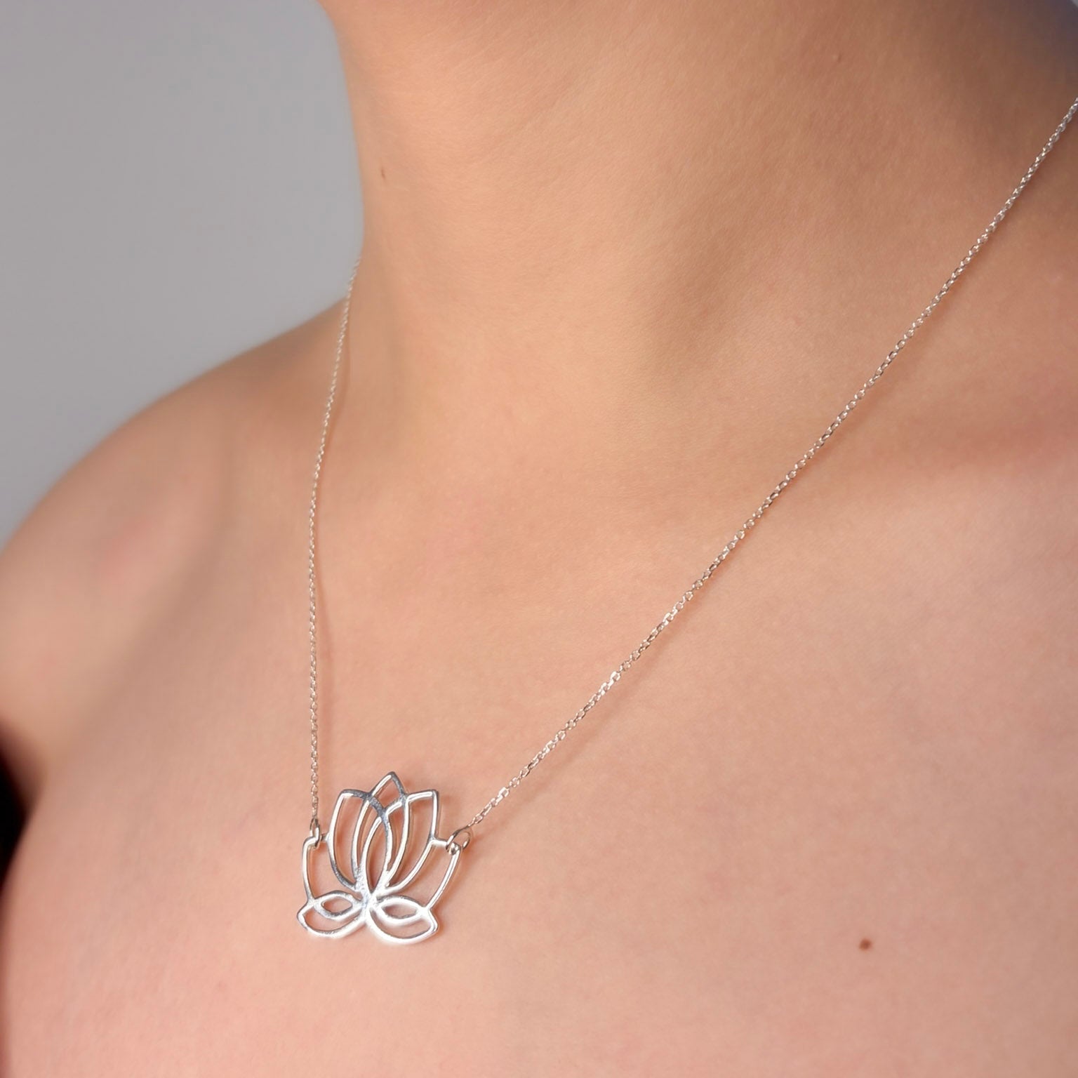 Silver lotus flower necklace on a person's neck against a neutral background