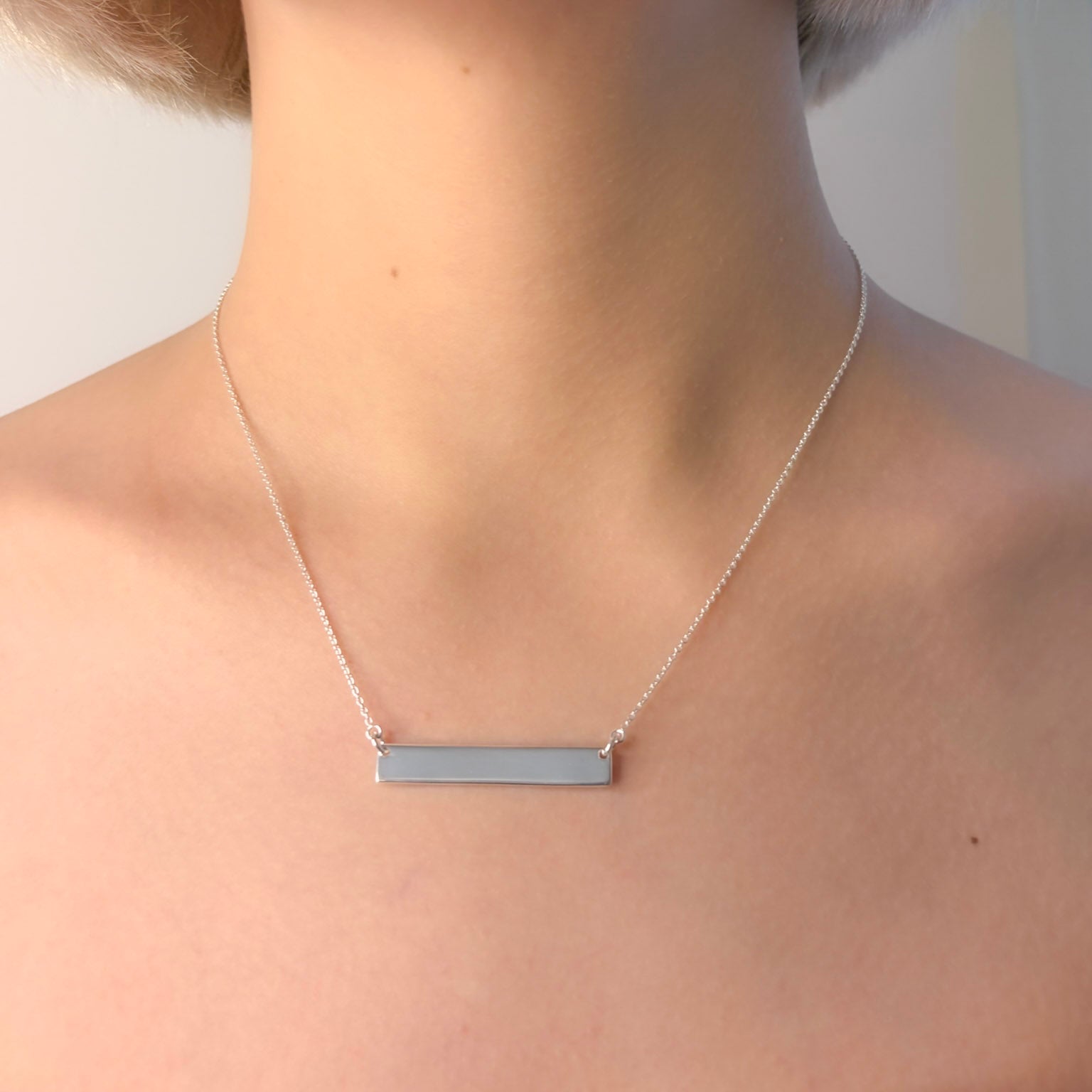 Silver bar necklace on a person against a neutral background