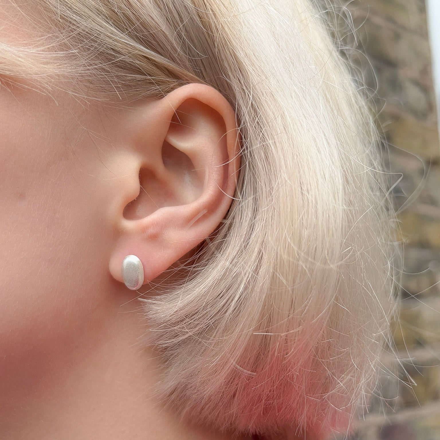 Close-up of an ear with an oval silver earring, blurred background