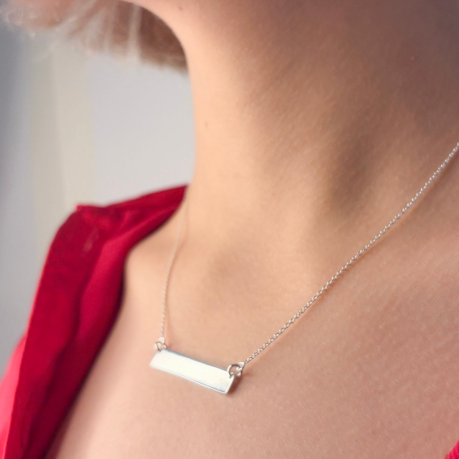 Silver necklace with a bar pendant on a person wearing a red garment.
