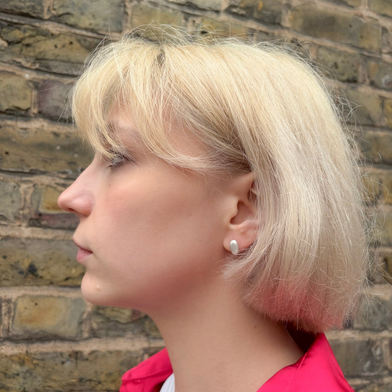 Woman with short blonde hair wearing a red jacket against a brick wall.