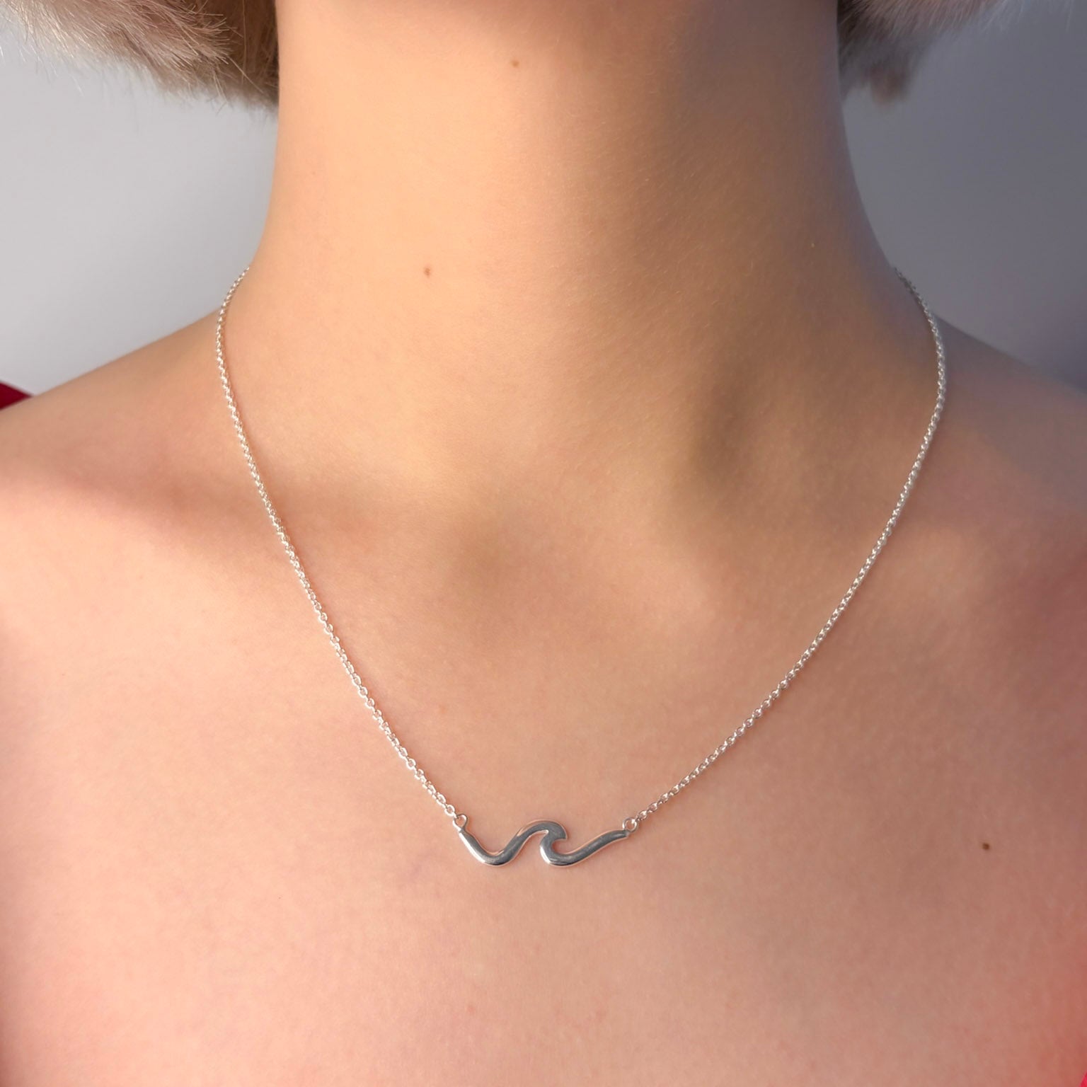 Silver necklace with a wave design on a person's neck against a neutral background