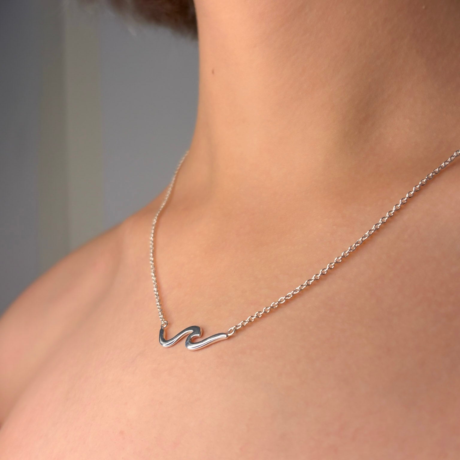 Silver wave necklace on a person's neck against a neutral background