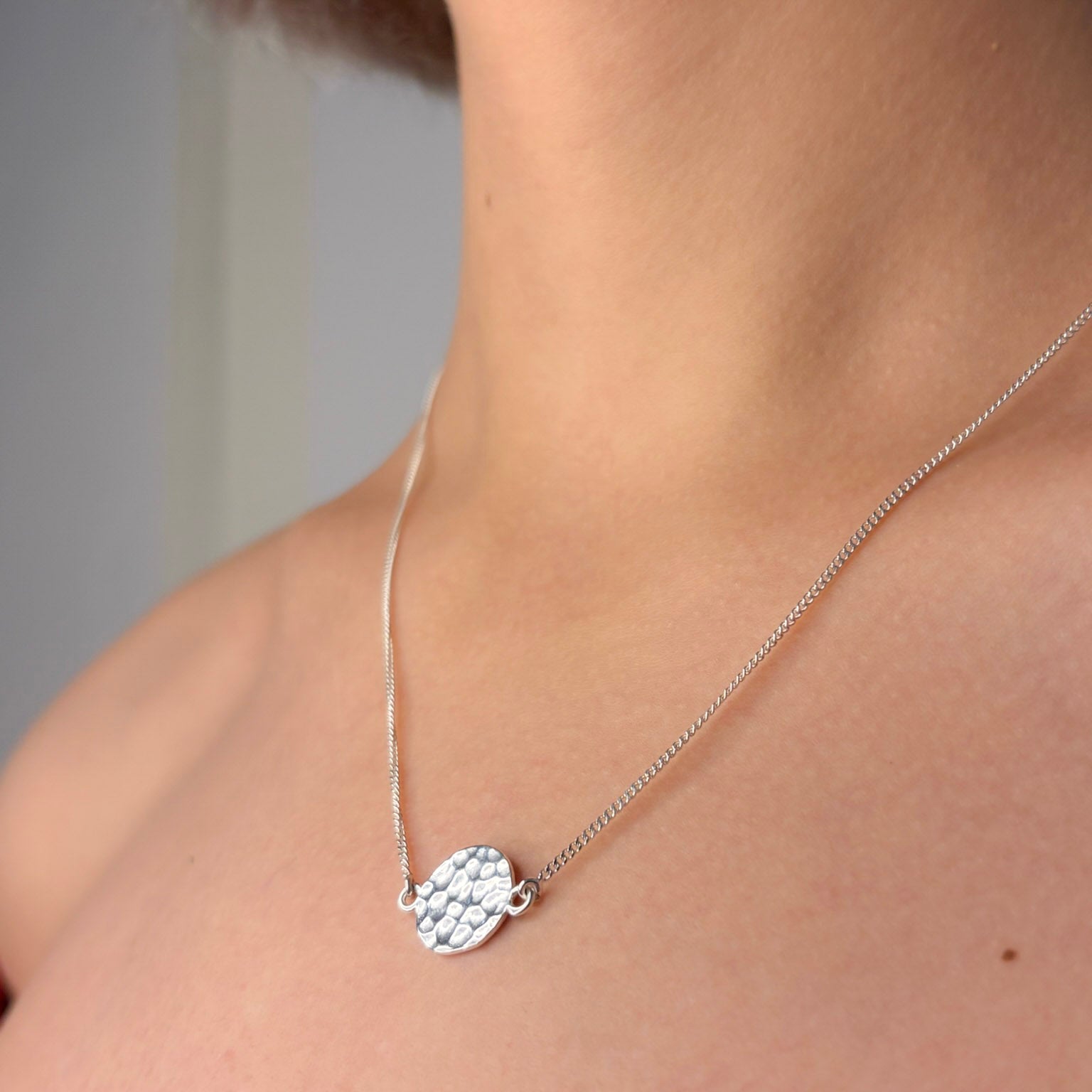Silver necklace with a unique pendant on a person's neck against a neutral background