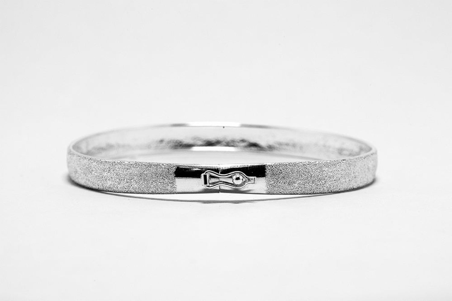 Silver bracelet with a textured band and engraved design on a white background
