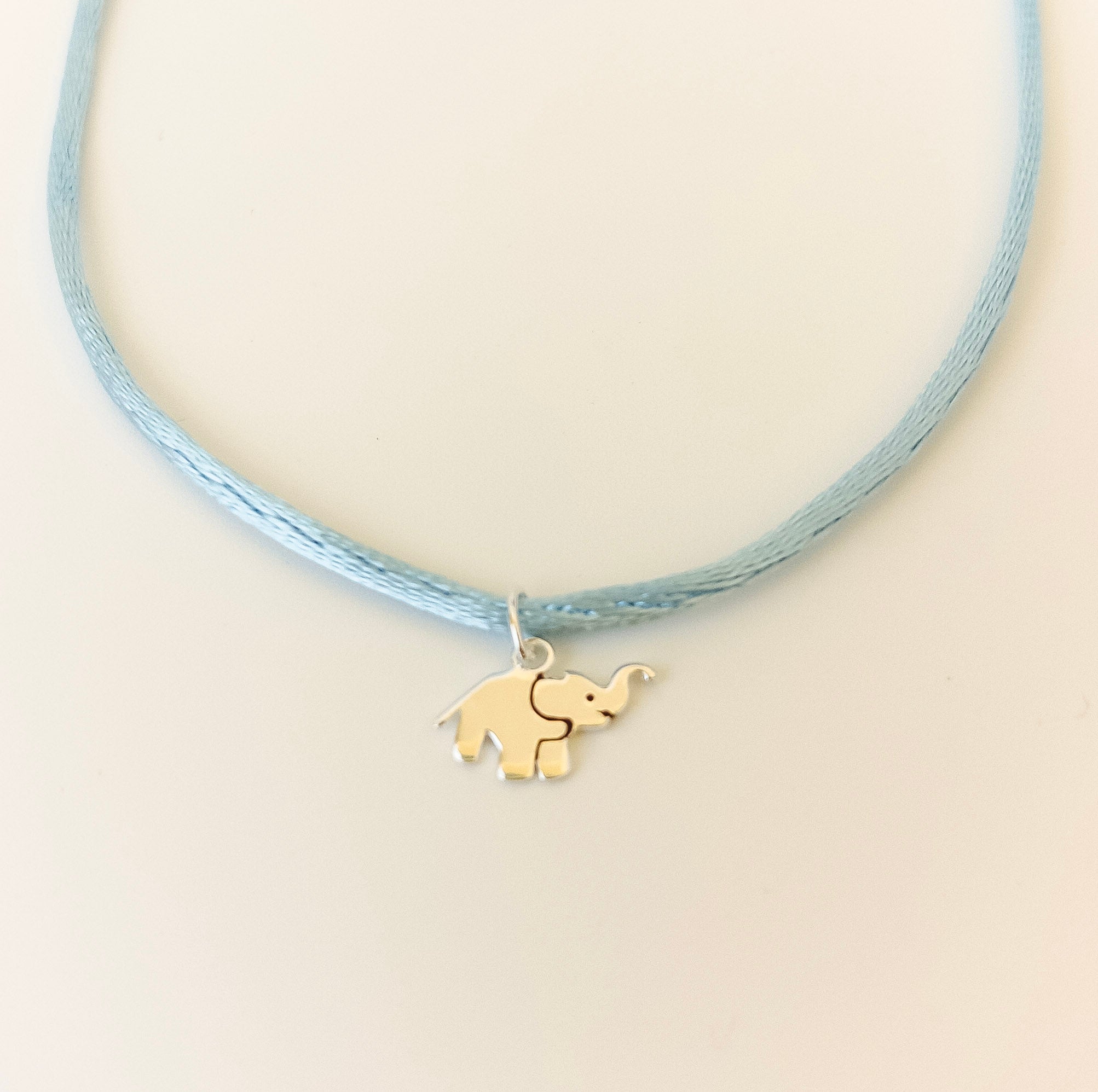 Necklace with a elephant charm on a light blue cord against a beige background