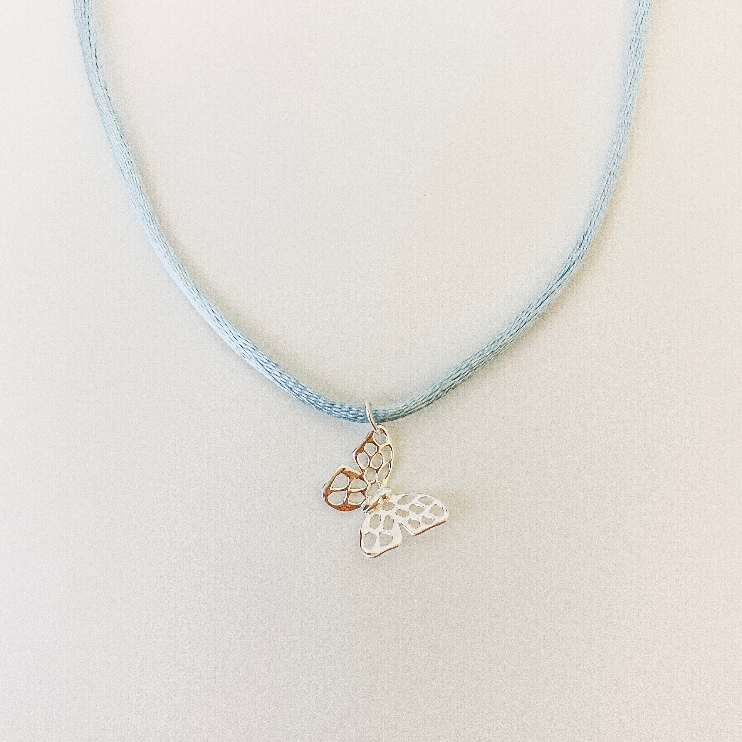Necklace with butterfly pendant on a light blue cord against a white background