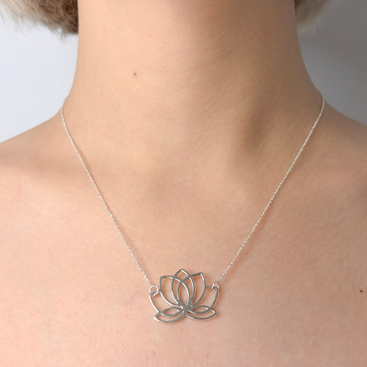 Silver lotus flower necklace on a person's neck against a neutral background