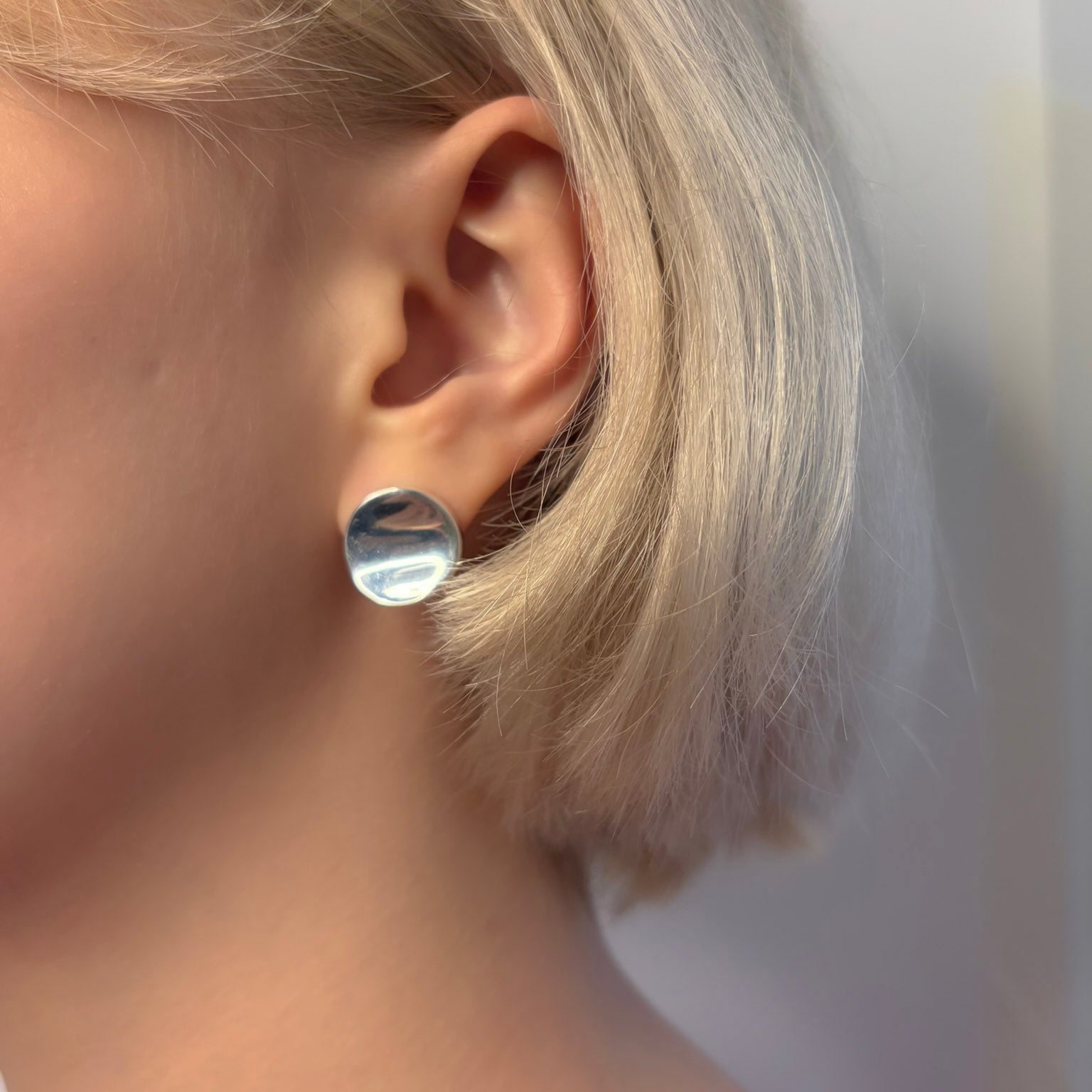 Close-up of an ear wearing a silver round earring with a blurred background