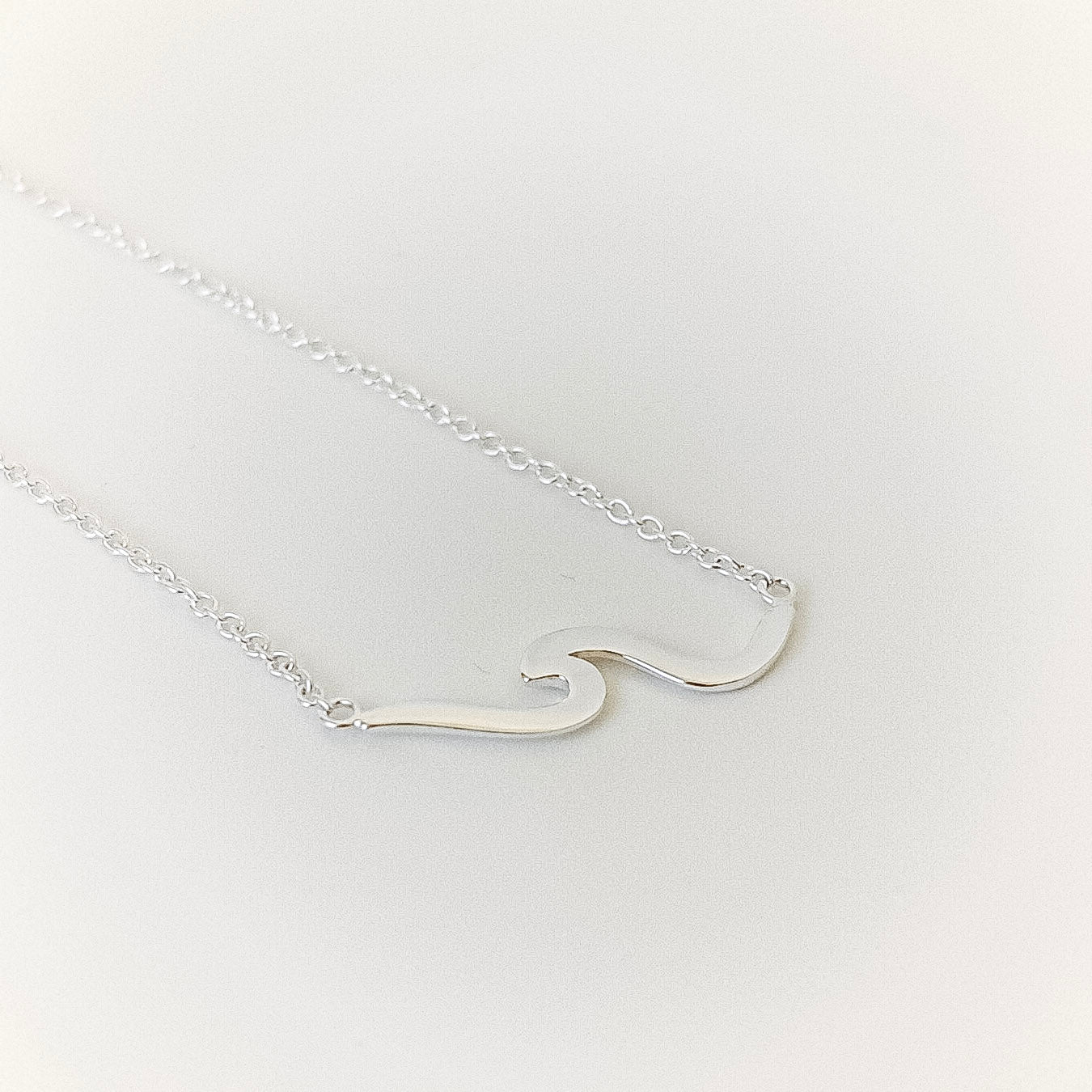 Silver wave-shaped pendant on a chain against a white background