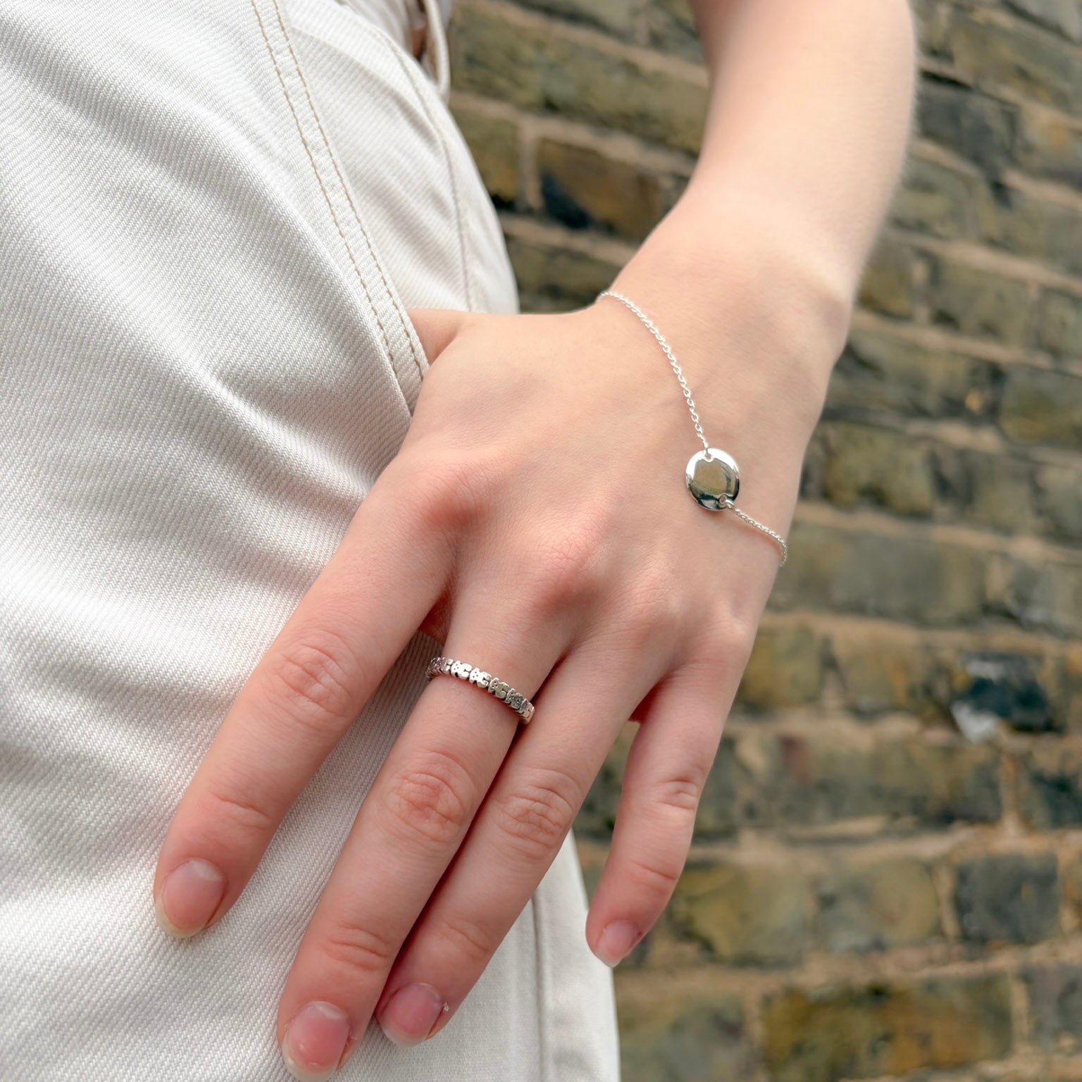 Close-up of a hand wearing a silver ring and bracelet against a brick wall.