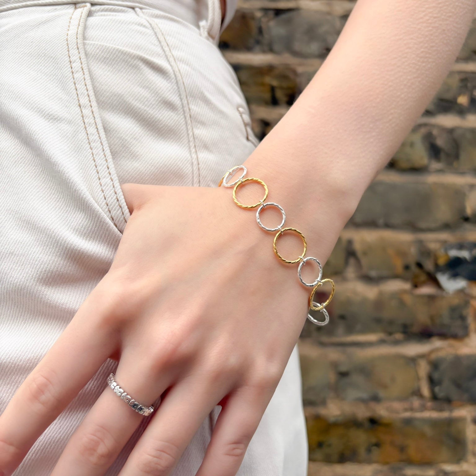 Close-up of a hand wearing a gold and silver bracelet against a stone wall background