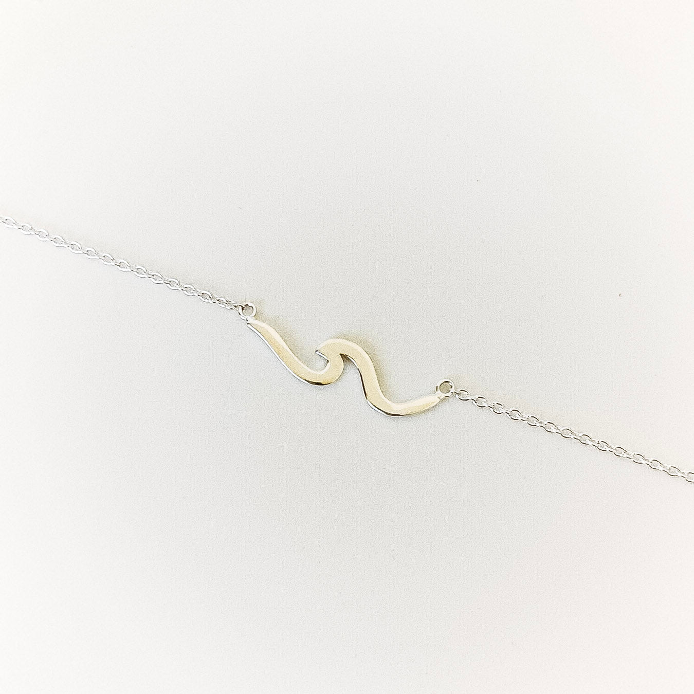 silver wave-shaped pendant on a chain against a white background