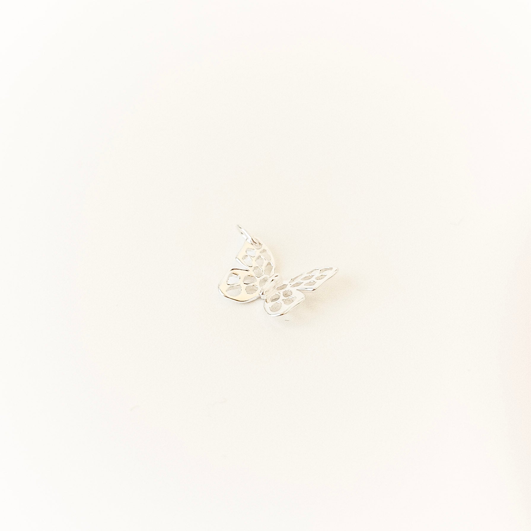 Small butterfly-shaped silver charm on a light beige background