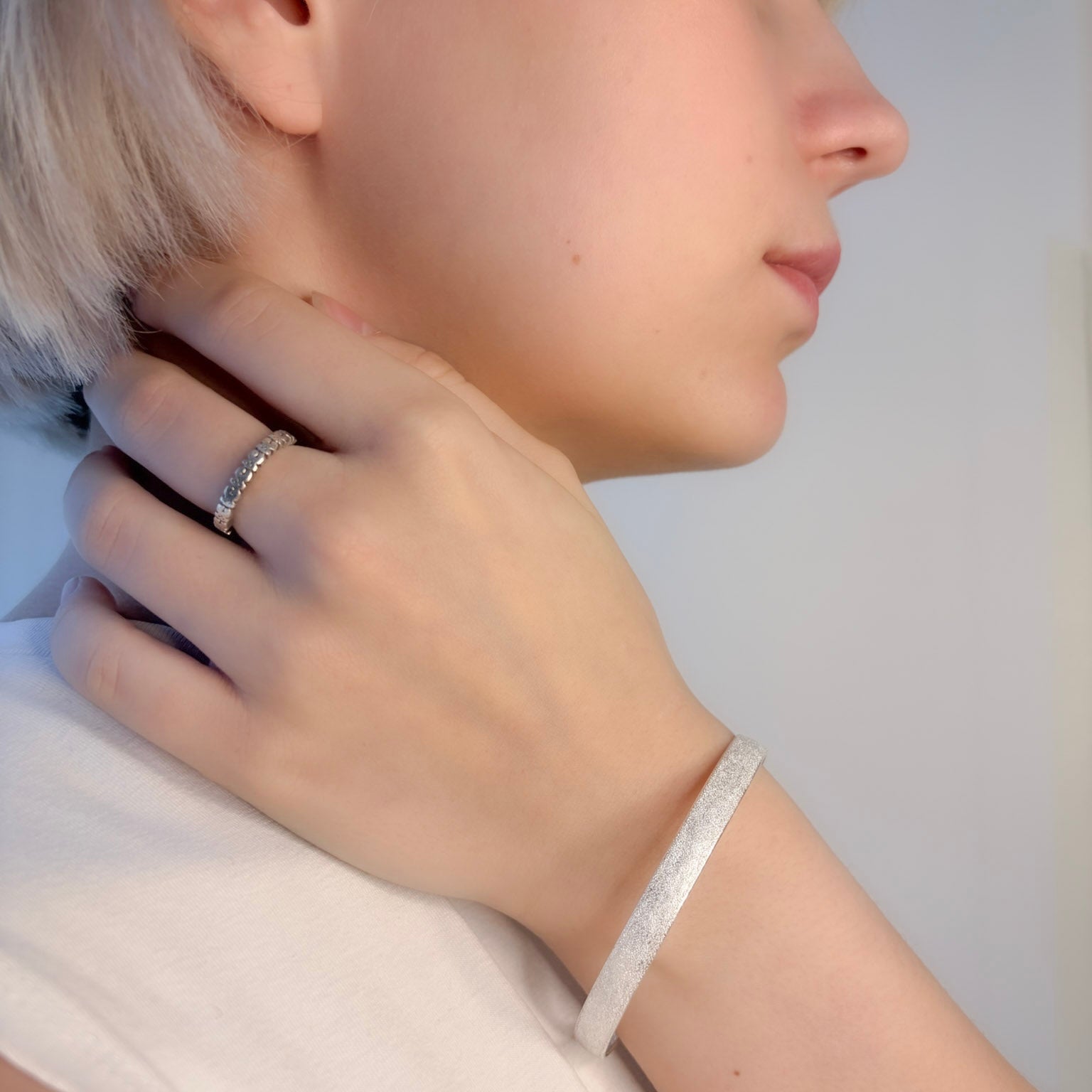 Close-up of a person wearing a silver ring and bracelet on a plain background