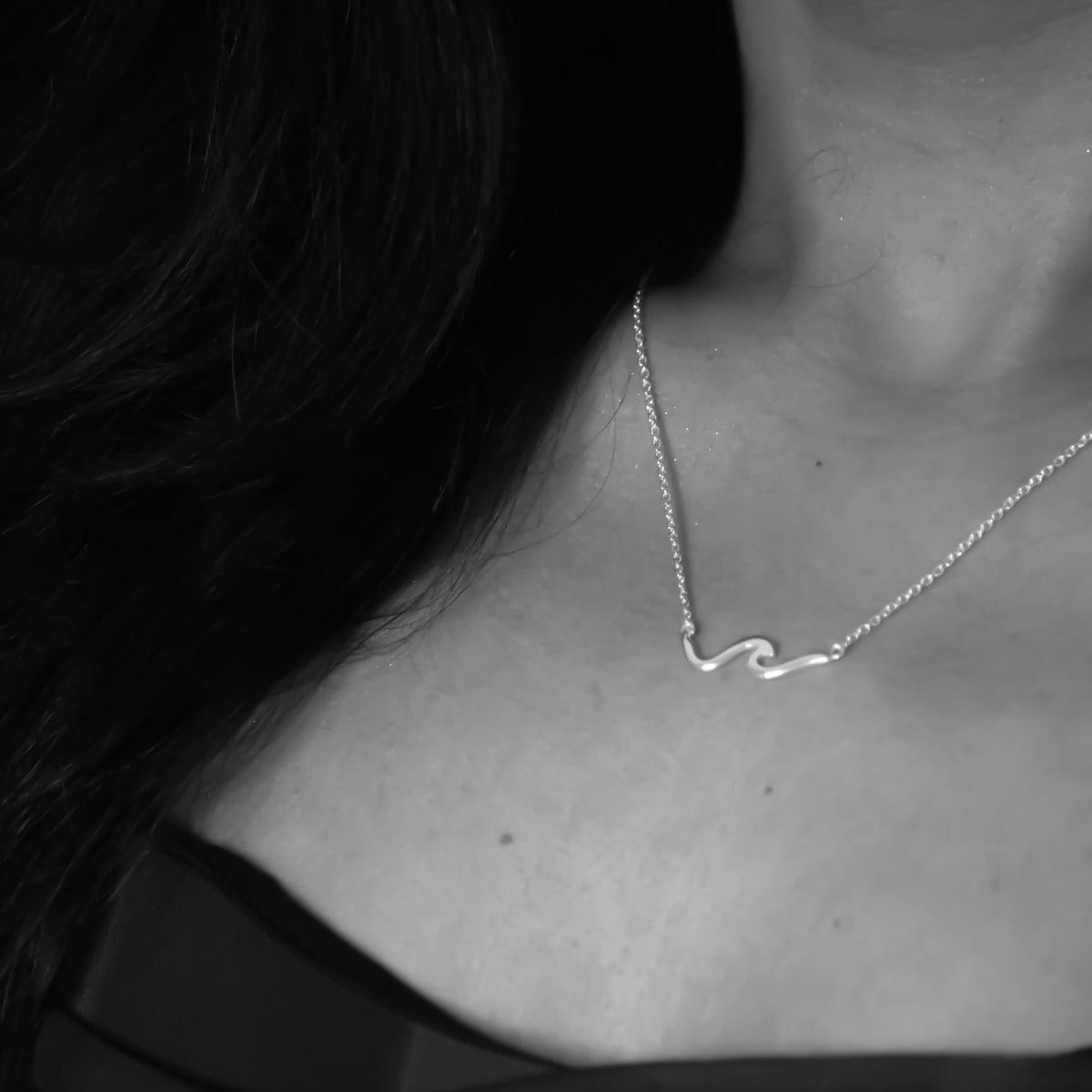 Silver wave necklace on a person's neck with a dark background