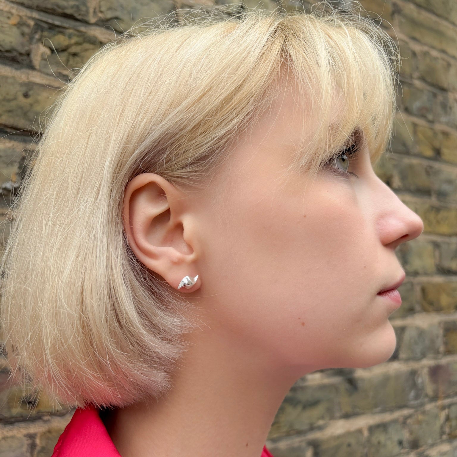 Profile of a person with blonde hair wearing a silver earring against a brick wall.