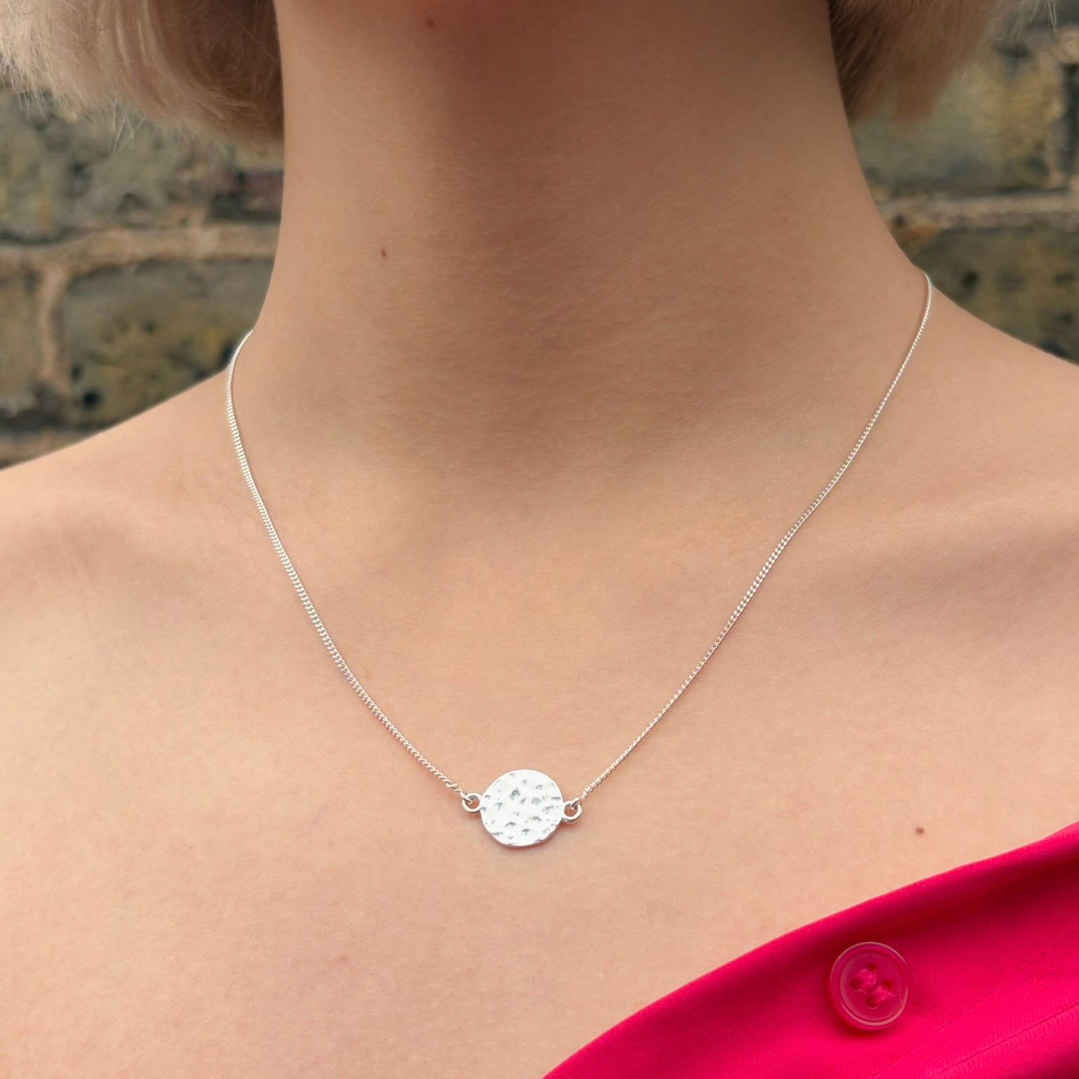 Silver necklace with a round pendant worn by a person against a blurred background