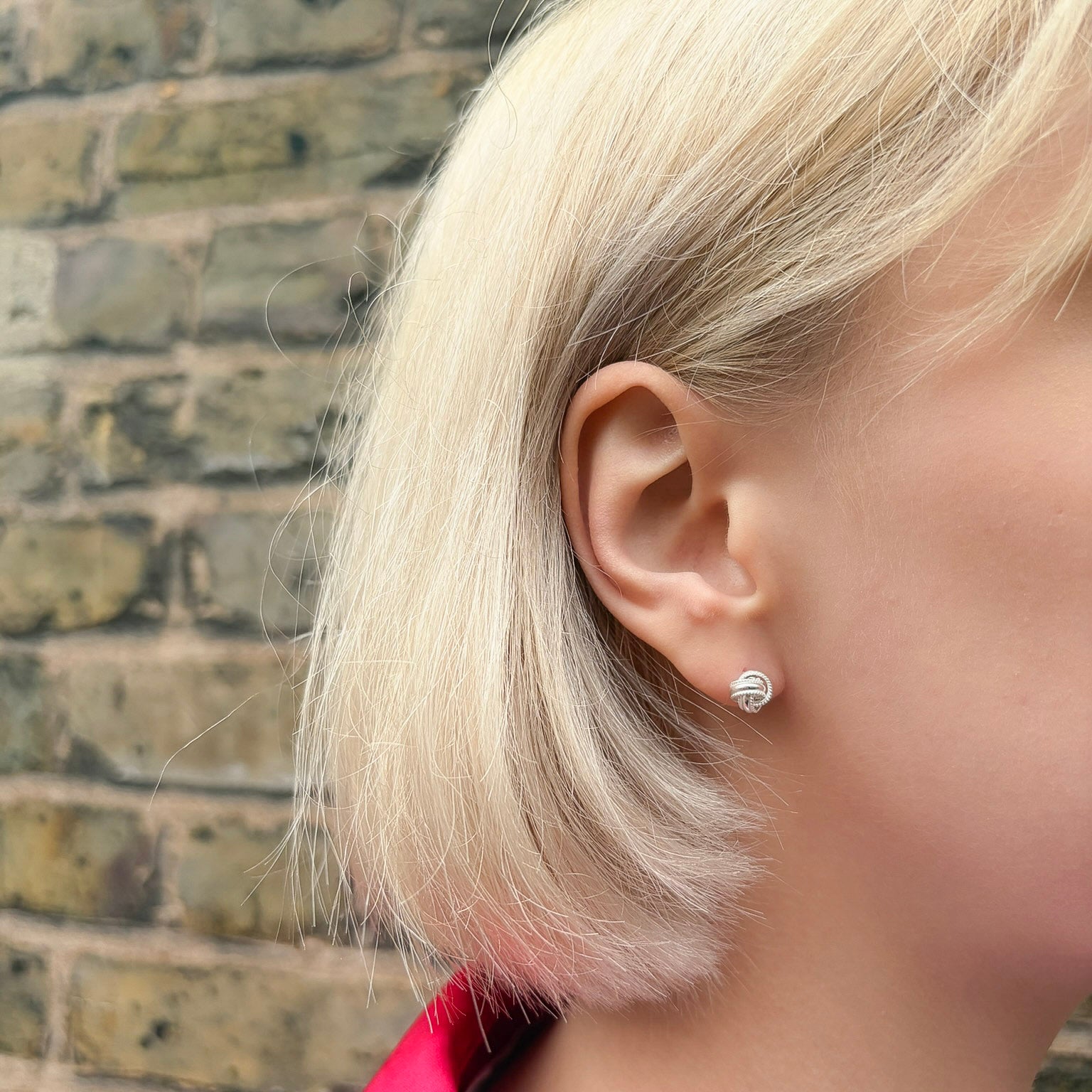 Close-up of a person wearing a silver earring with a brick wall background