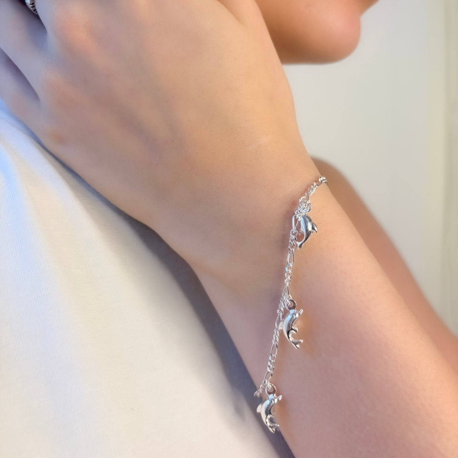 Silver bracelet with dolphin charms on a wrist against a light background