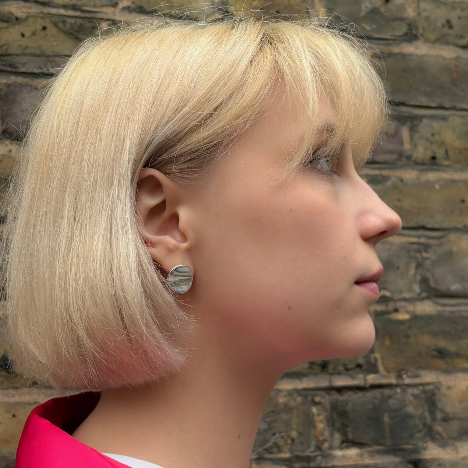 Profile of a person with blonde hair wearing statement silver disc studs