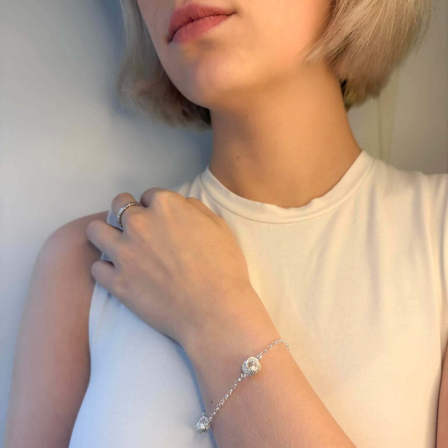 Person wearing a silver bracelet with a clear gemstone on a plain background