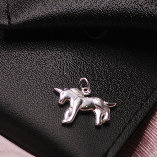 Silver unicorn pendant on a black leather surface