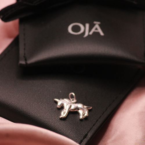 Silver dog-shaped pendant on a black surface with 'Oja' branding.